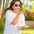 A woman celebrating Holi festival outdoors, blowing vibrant colors with a smile.