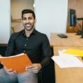 Smiling businessman holding documents at his desk, embracing productivity in a modern office.