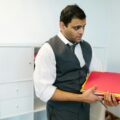 Male office worker in formal attire holding colorful folders in a modern office space.